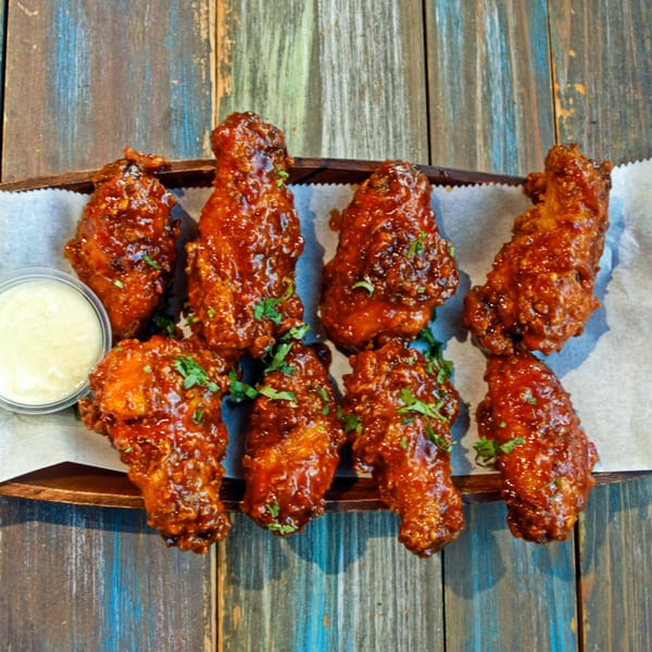 Eight Desi Bistro chicken wings, glazed in a rich sauce, with a side of dipping sauce.