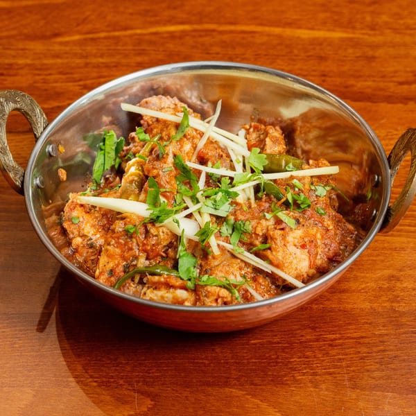 Desi Bistro's chicken karahi, garnished with ginger and cilantro, in a traditional metal bowl.