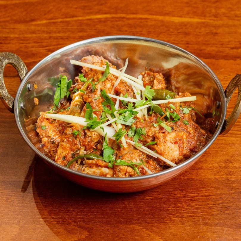 Desi Bistro's chicken karahi, garnished with ginger and cilantro, in a traditional metal bowl.