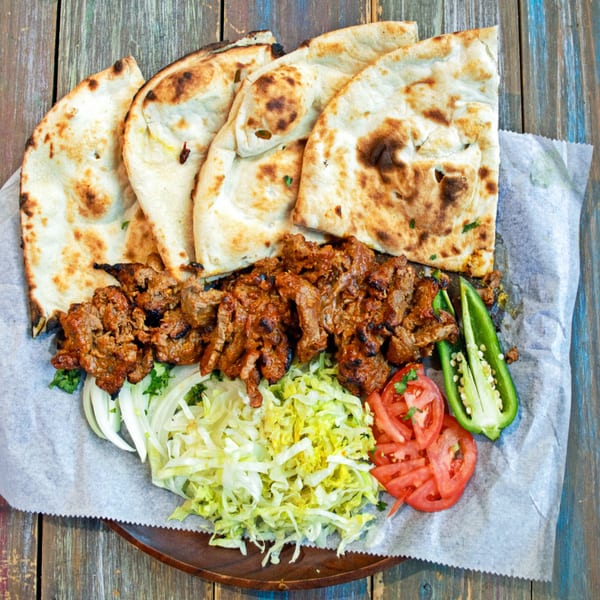 Desi Bistro's Indian dish with grilled meat, naan bread, sliced tomatoes, lettuce, and green peppers.