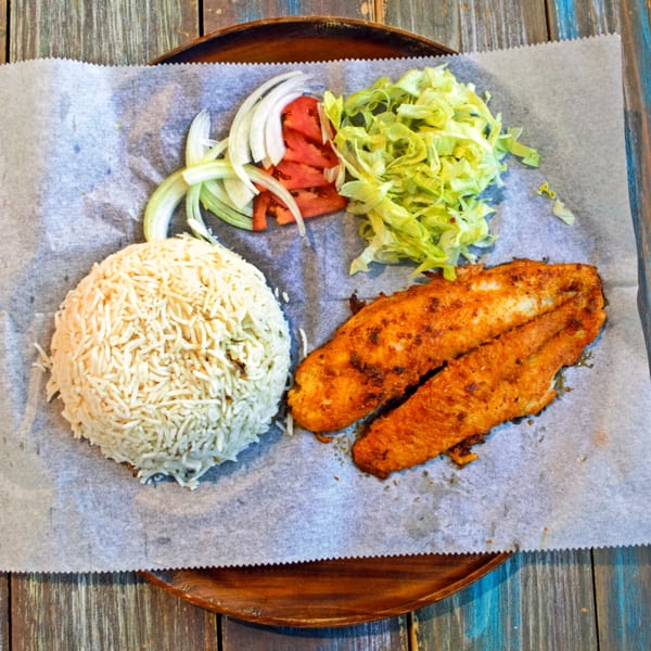 Desi Bistro's fried fish with rice, sliced onions, tomatoes, and shredded lettuce on a wooden plate.