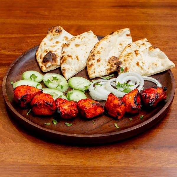 Desi Bistro's chicken tikka, naan, cucumber, and onion on a wooden plate.