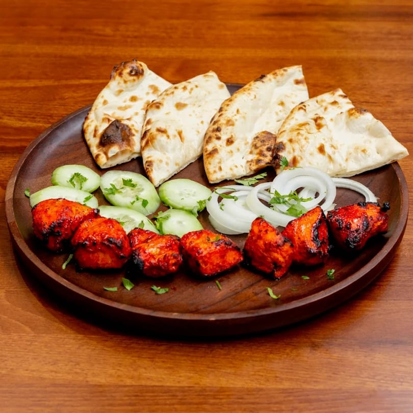 Desi Bistro's chicken tikka, naan, cucumber, and onion on a wooden plate.