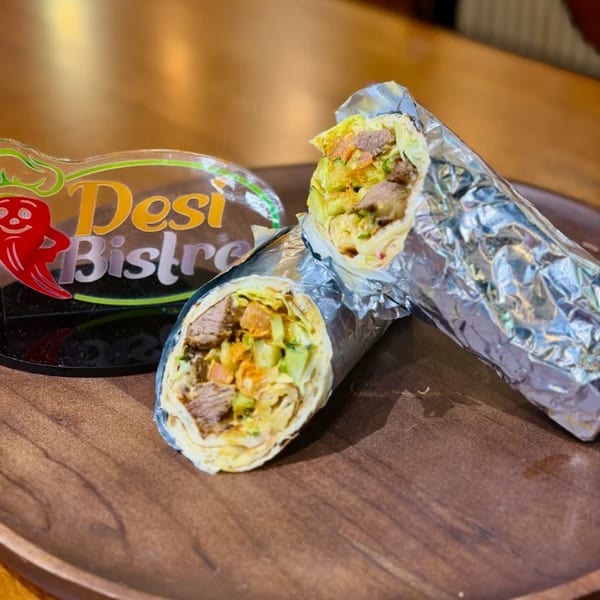 Two Desi Bistro Indian wraps, filled with meat and vegetables, on a wooden tray.